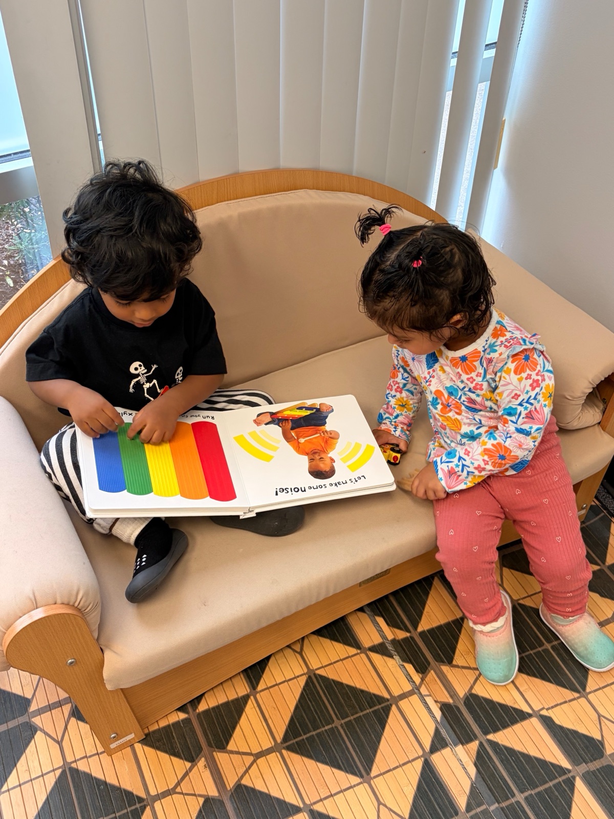 two toddlers sharing a book on the classroom couch